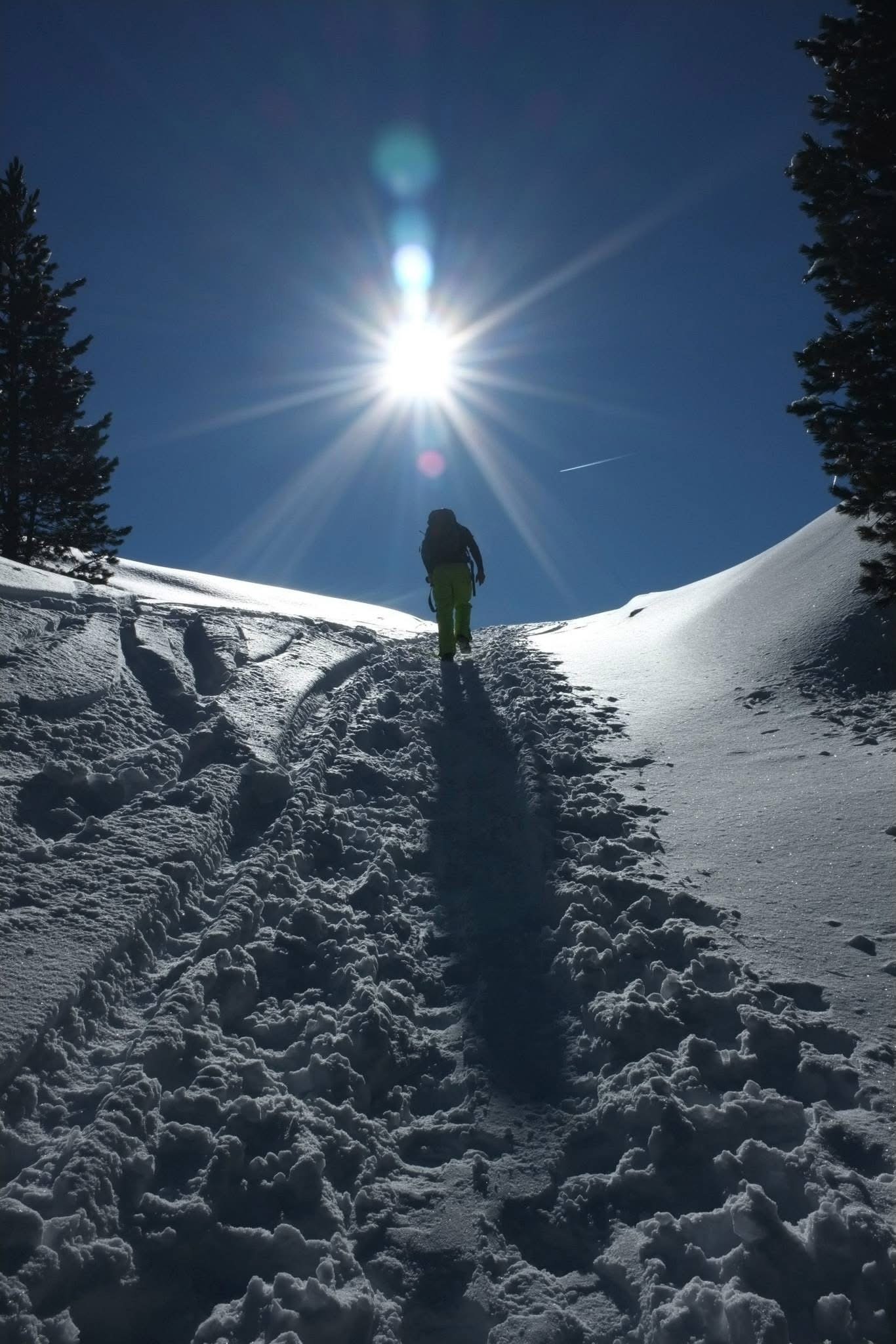Backlit hiker walking uphill through deep snow in the Dolomites with the sun overhead
