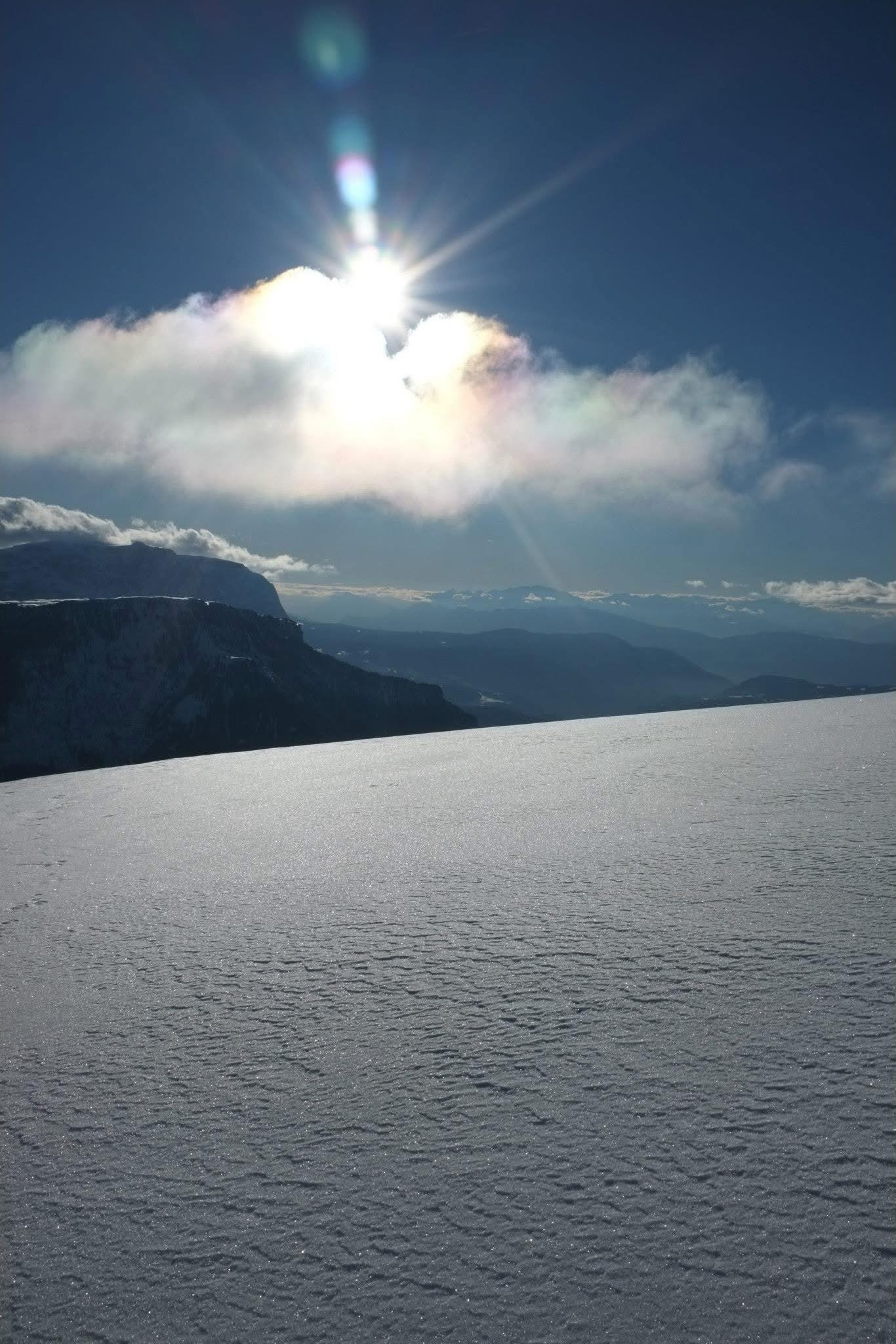 Bright winter sun shining over a snow-covered plateau in the Dolomites with soft clouds and distant mountains