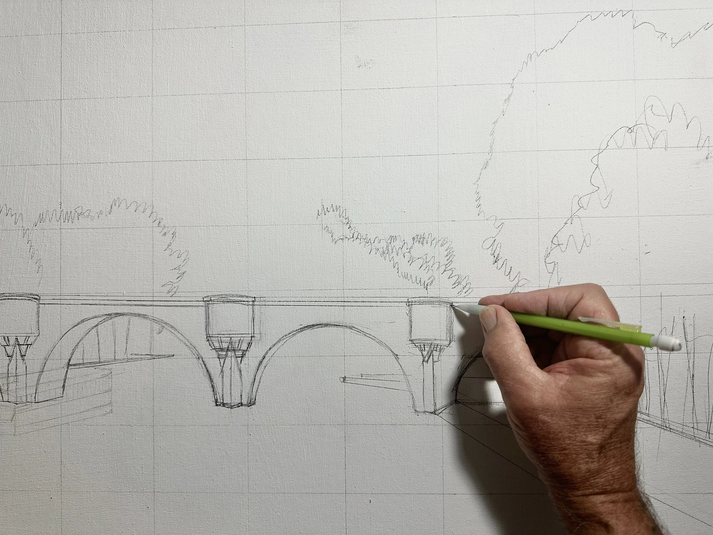 Hand sketching a bridge with arches and landscape in the background on drawing paper.