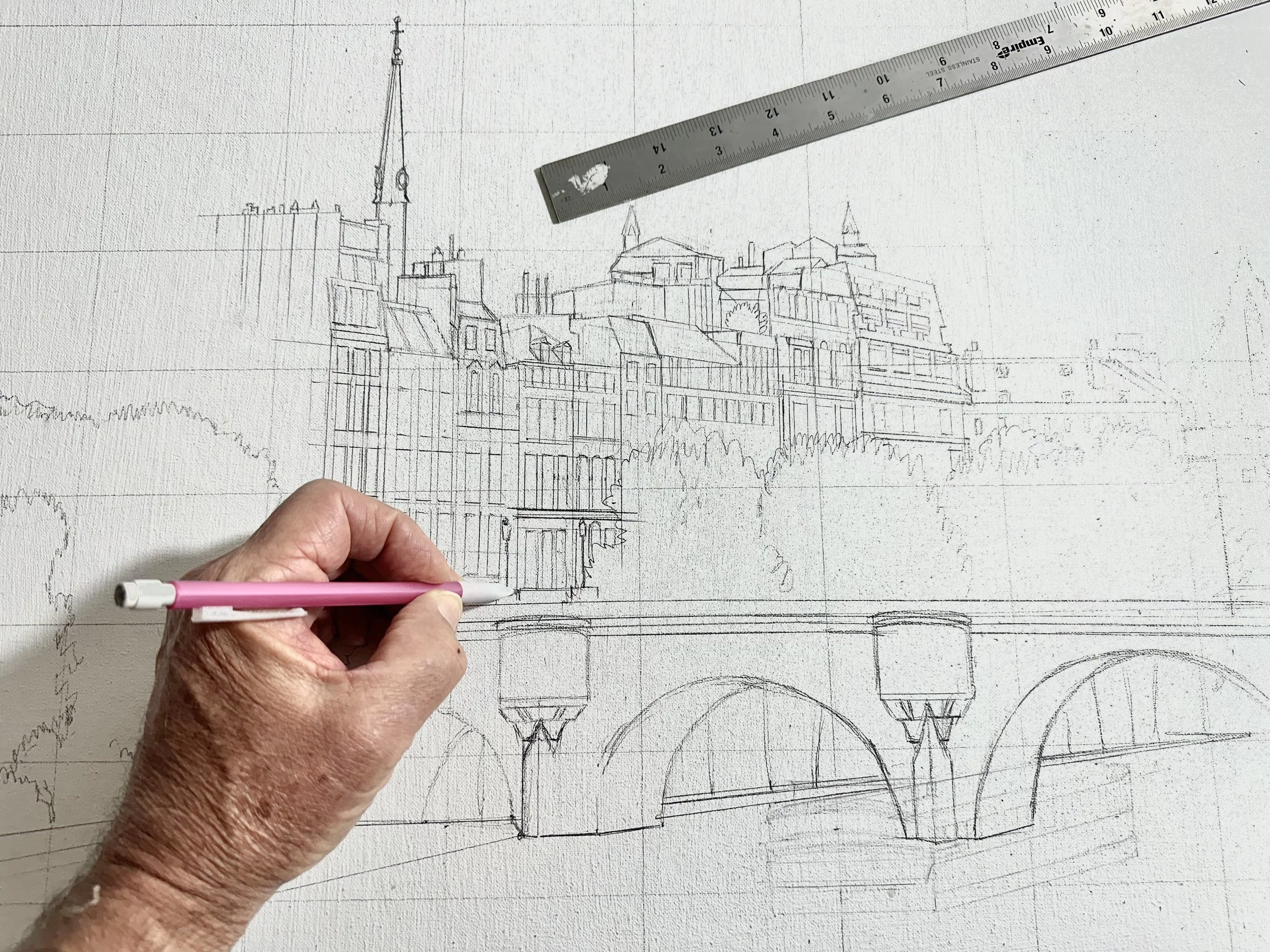 An artist sketching a perspective drawing of the Pont Neuf bridge and Parisian buildings. A metal ruler and pencil are visible over a canvas marked with a light graphite grid.