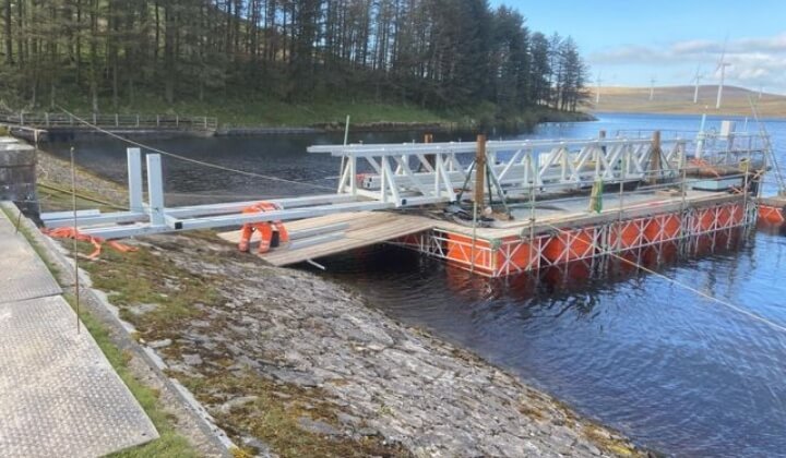 Floating platform with steel bridge sections positioned on Penwhapple Reservoir during construction work.