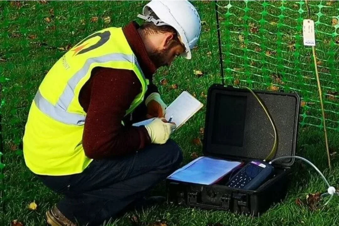 Geotechnical engineer conducting Phase 2 site investigation with gas and groundwater monitoring equipment on grass field.