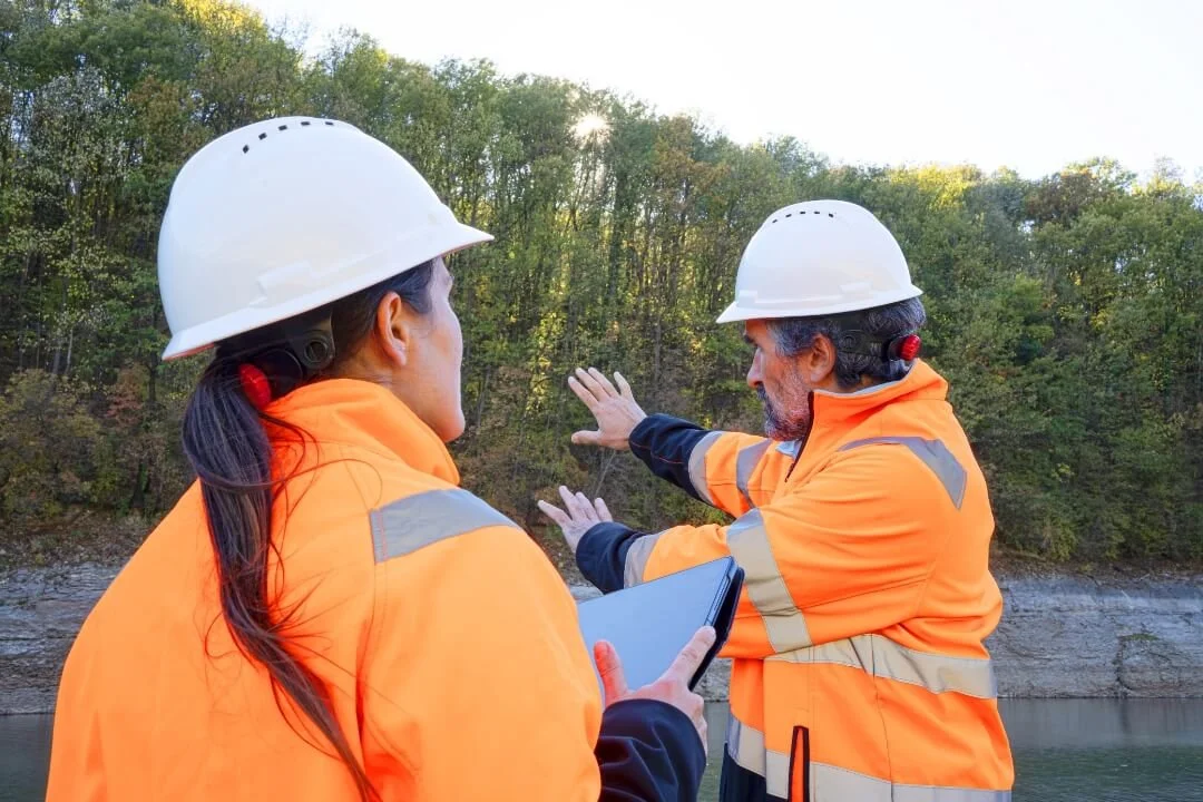 Two engineers on a riverbank conducting a site walkover survey, noting vegetation, slopes and access constraints.