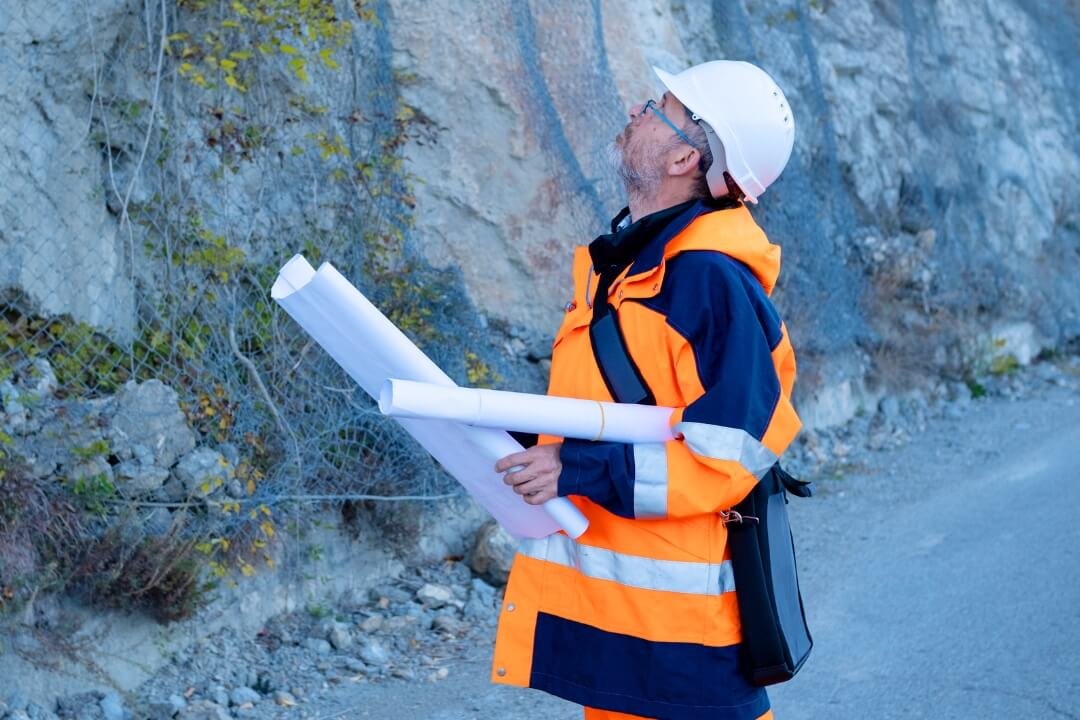 Engineer inspecting a rock face with plans during a site walkover survey to assess slope stability.