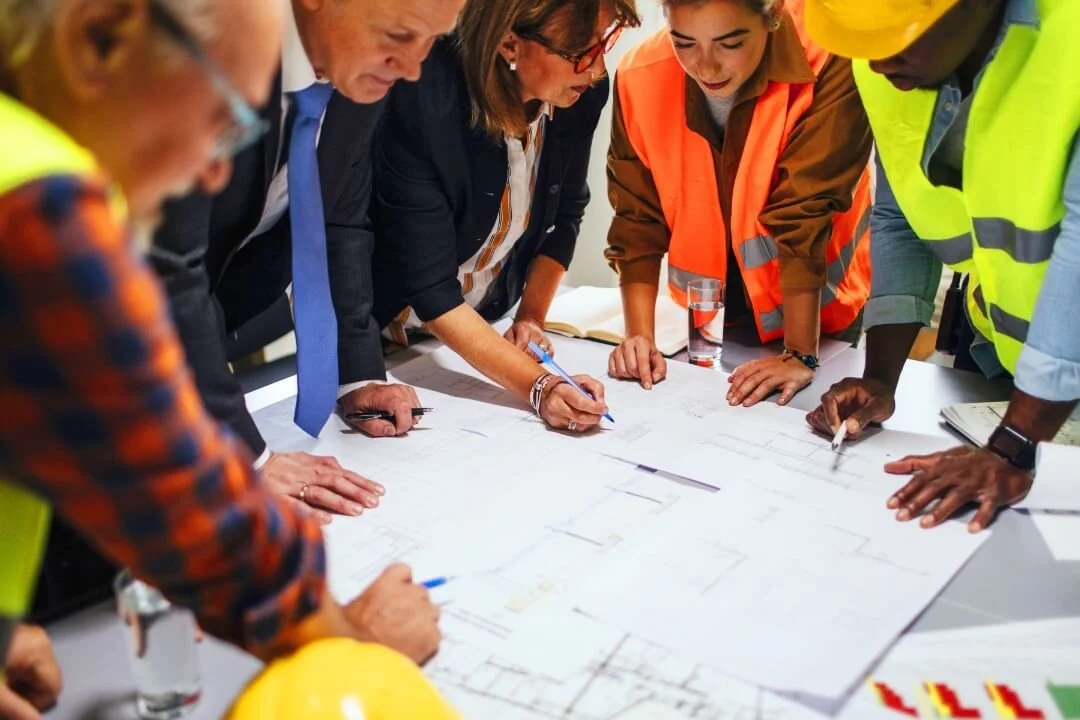 Team of engineers and consultants reviewing site plans during a Phase 1 Desk Study meeting.