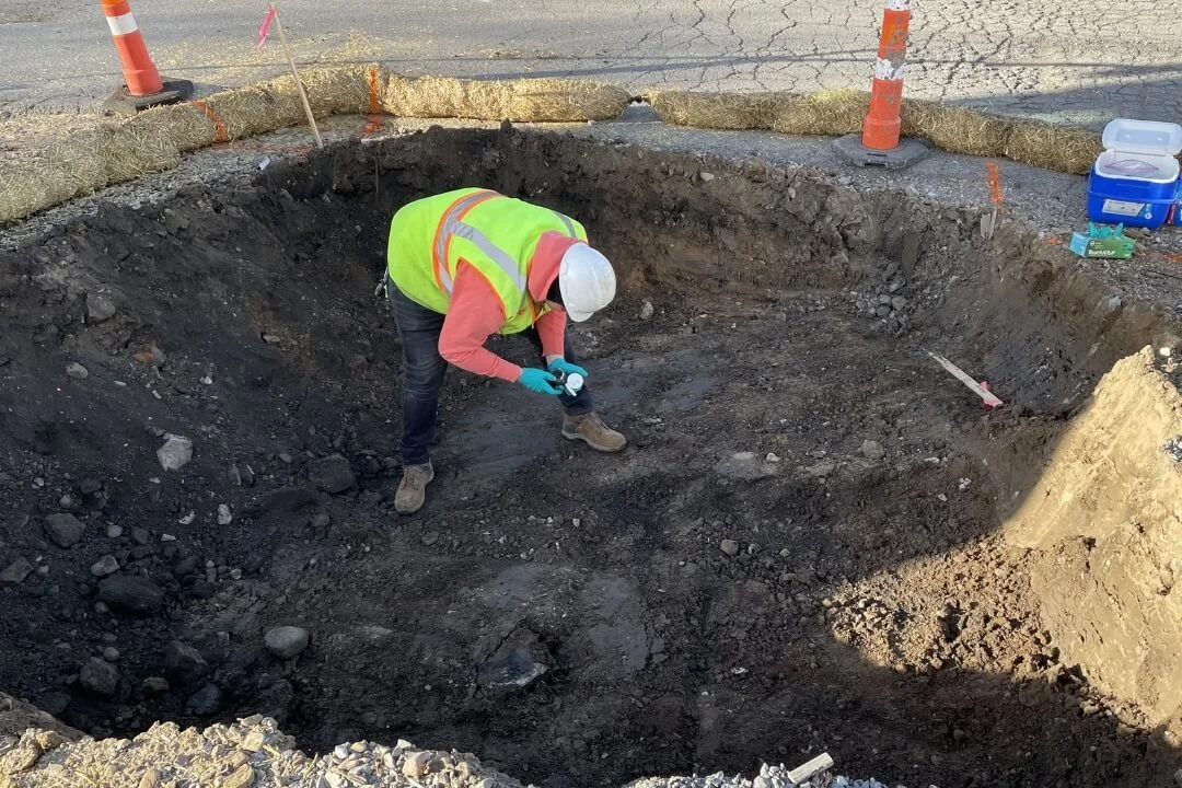 Engineer conducting soil sampling in an excavation pit during geological assessment.