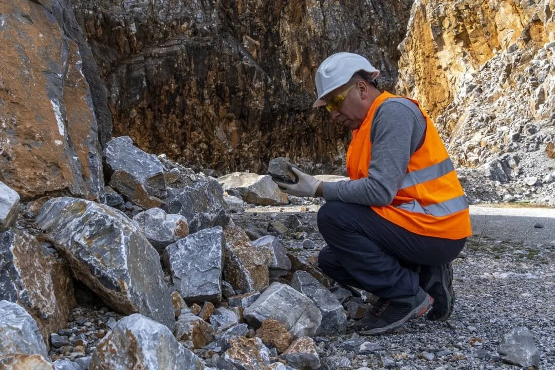 Geologist examining rock outcrop and collecting samples for Phase 2 geotechnical assessment.