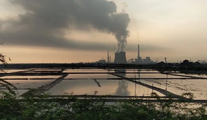 Industrial site emitting smoke near water bodies during environmental pollution assessment for land remediation