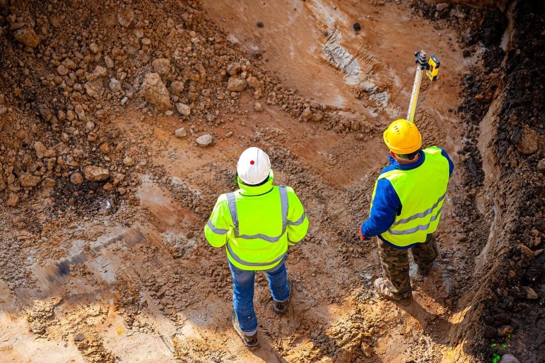 Engineers inspecting and measuring an open trial pit to log strata during a Phase 2 investigation.