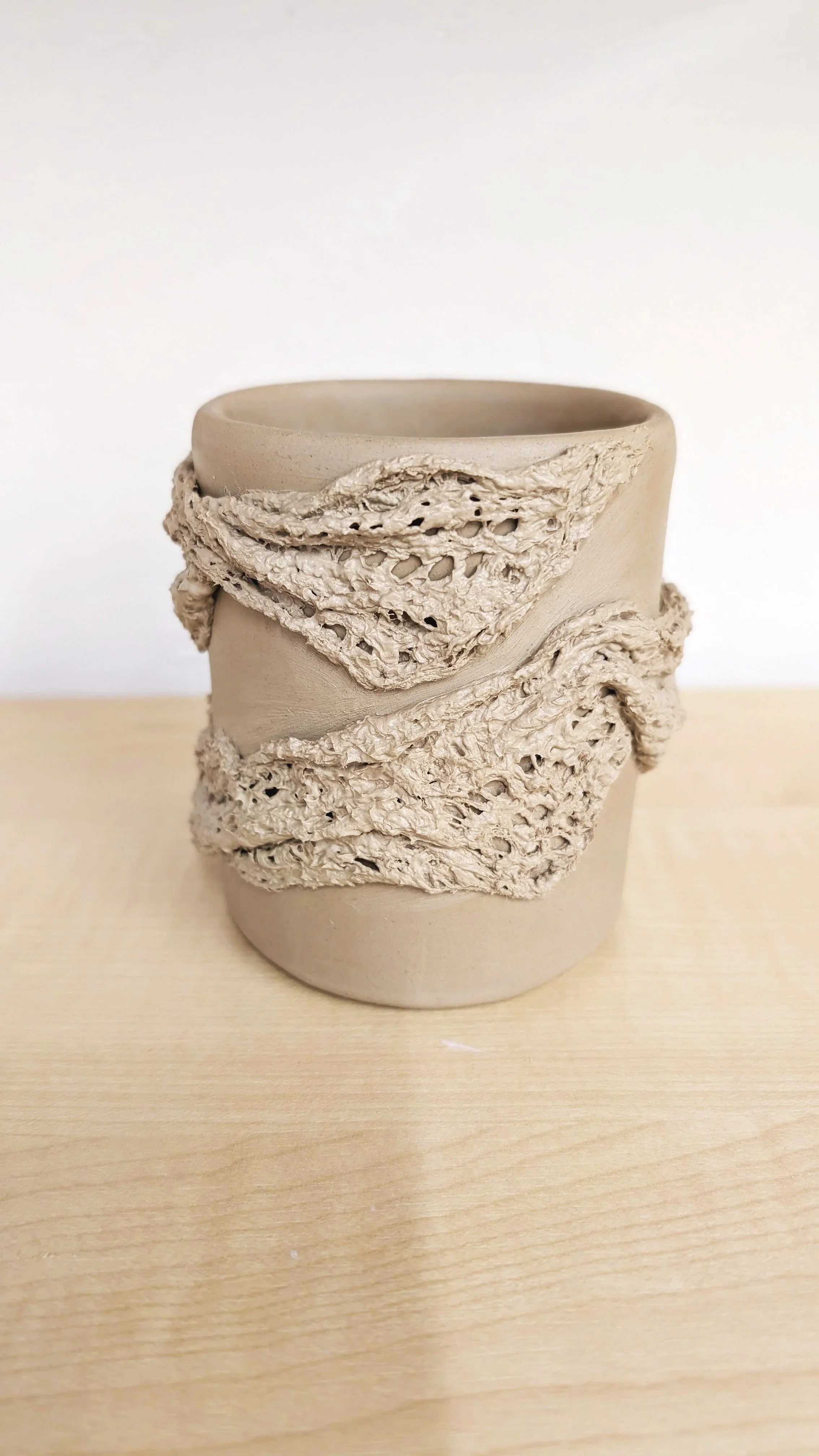 Poterie représentant un mug sans anse réalisé en terre blanche et décoré d'un effet de tissu drapé.