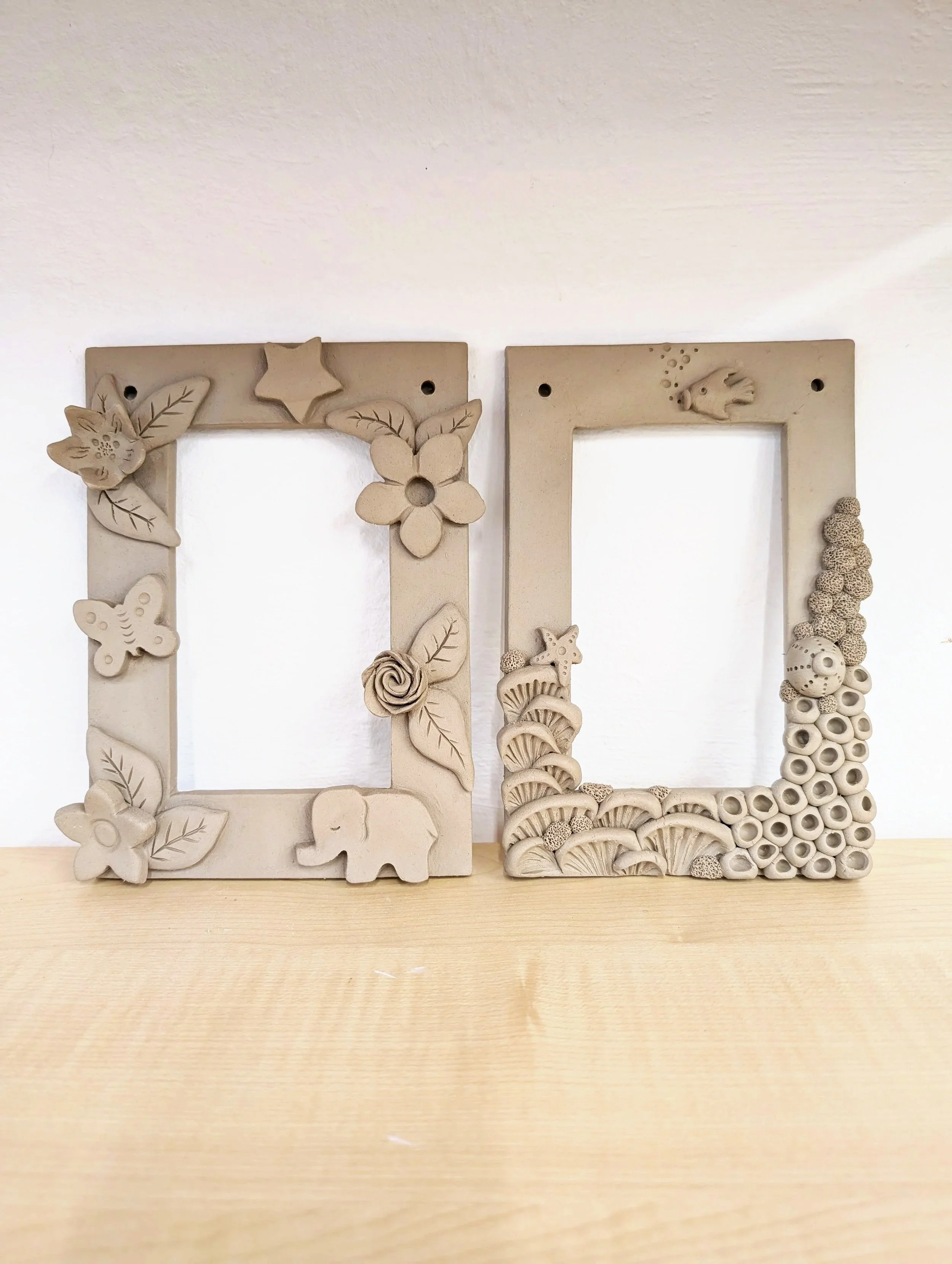 Lot de deux cadres photo en céramique beige avec décorations de fleurs, d'animaux et d'éléments marins, à suspendre au mur à l'aide d'une cordelette passant par deux petits trous.