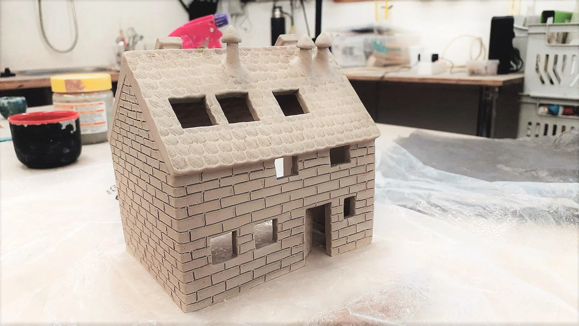 Petite maison en céramique avec travail de texture sur les murs (briques) et le toit (tuiles).