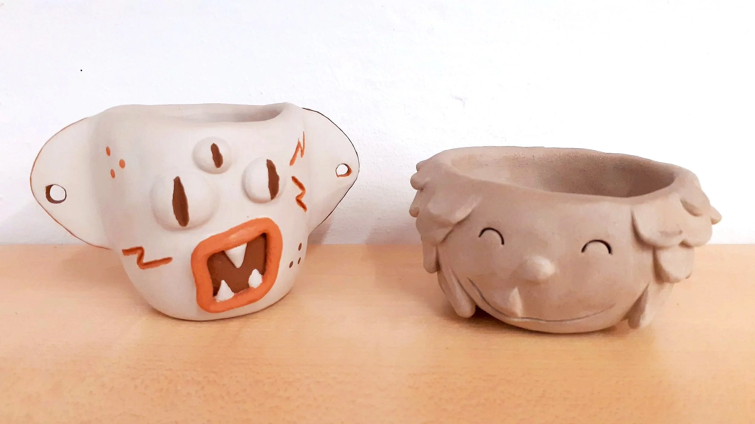 Poteries représentant des petits cache-pots en terre blanche, décorés de visages de monstres rigolos et légèrement peints de rouge et de brun foncé.