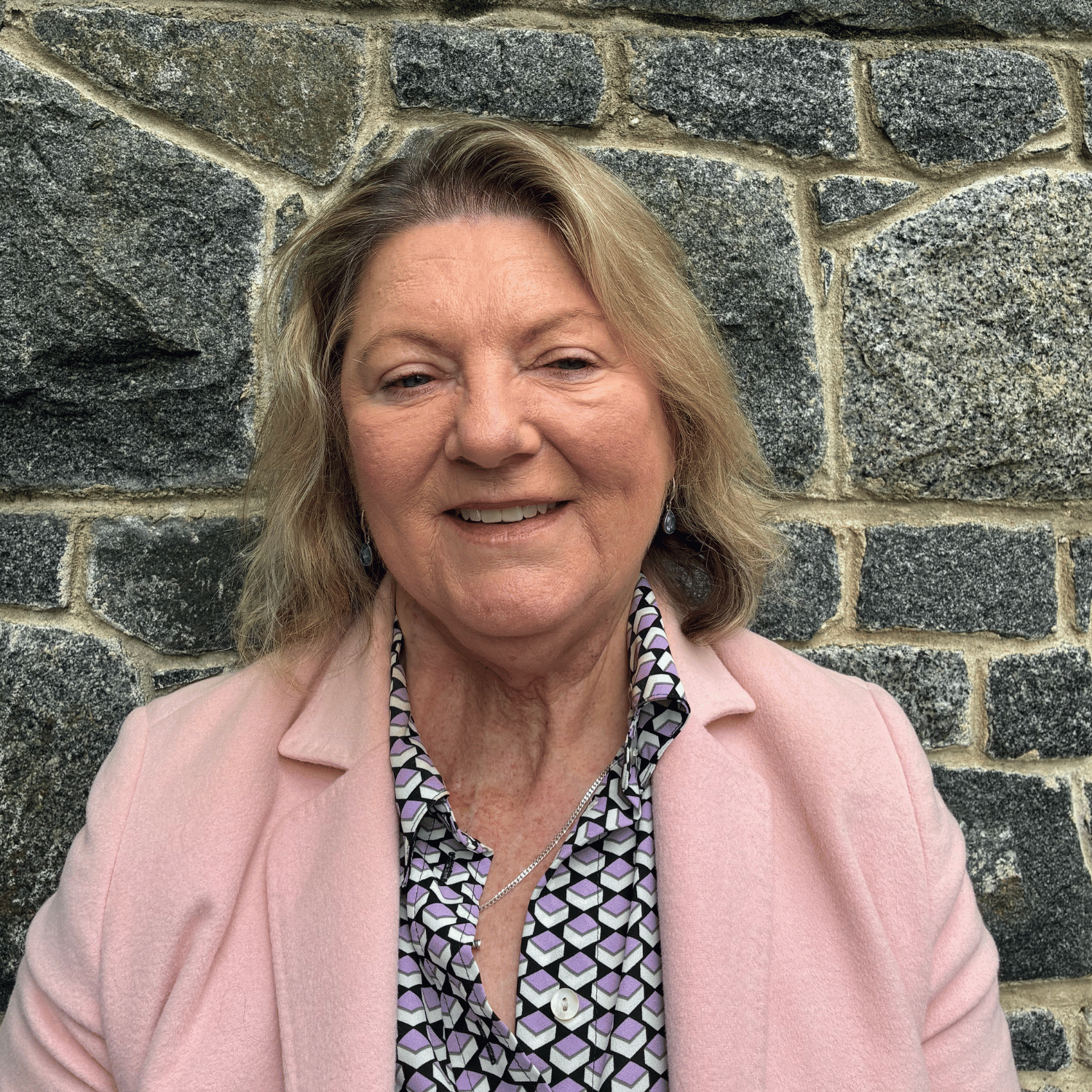 A smiling woman with blonde hair in an office or conference room setting.