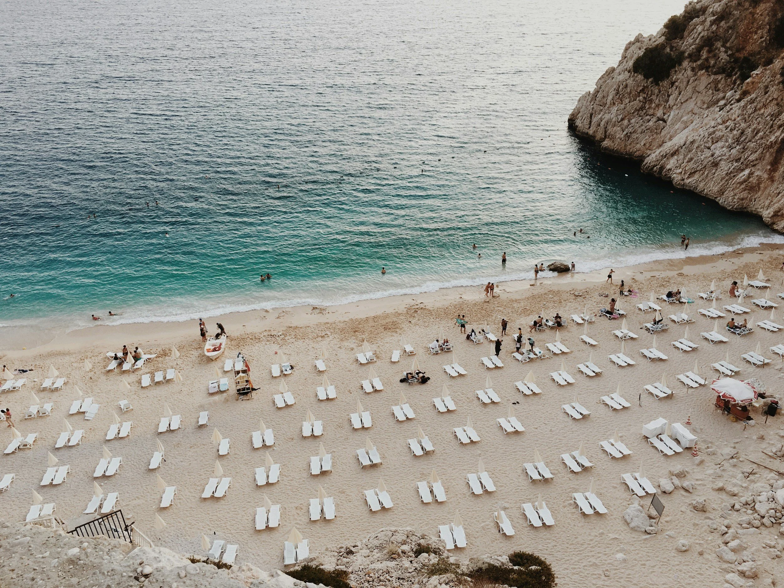 Beach with turquoise water, white sand, beach chairs, umbrellas, and people swimming and relaxing.