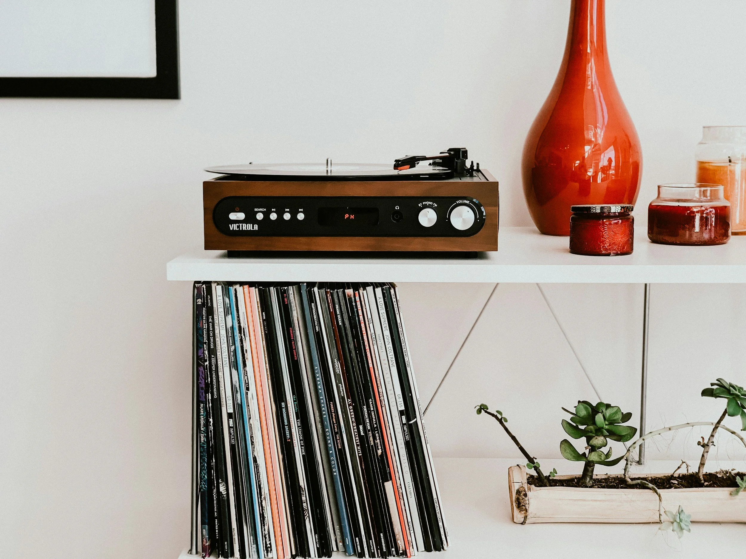 Shelf with a record player, vinyl records, and decorative vases and candles.
