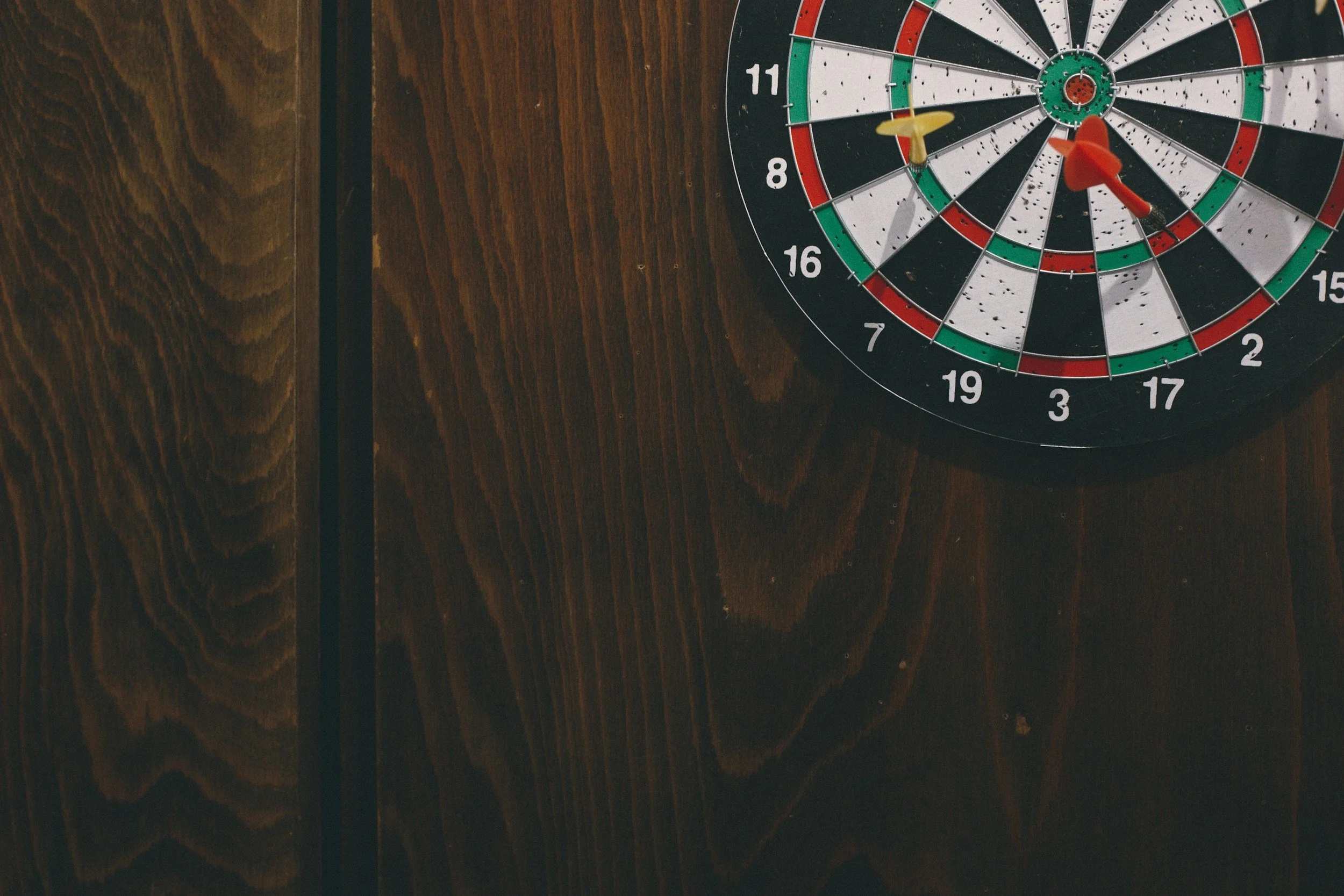 Dartboard with yellow and red darts on a wooden wall.