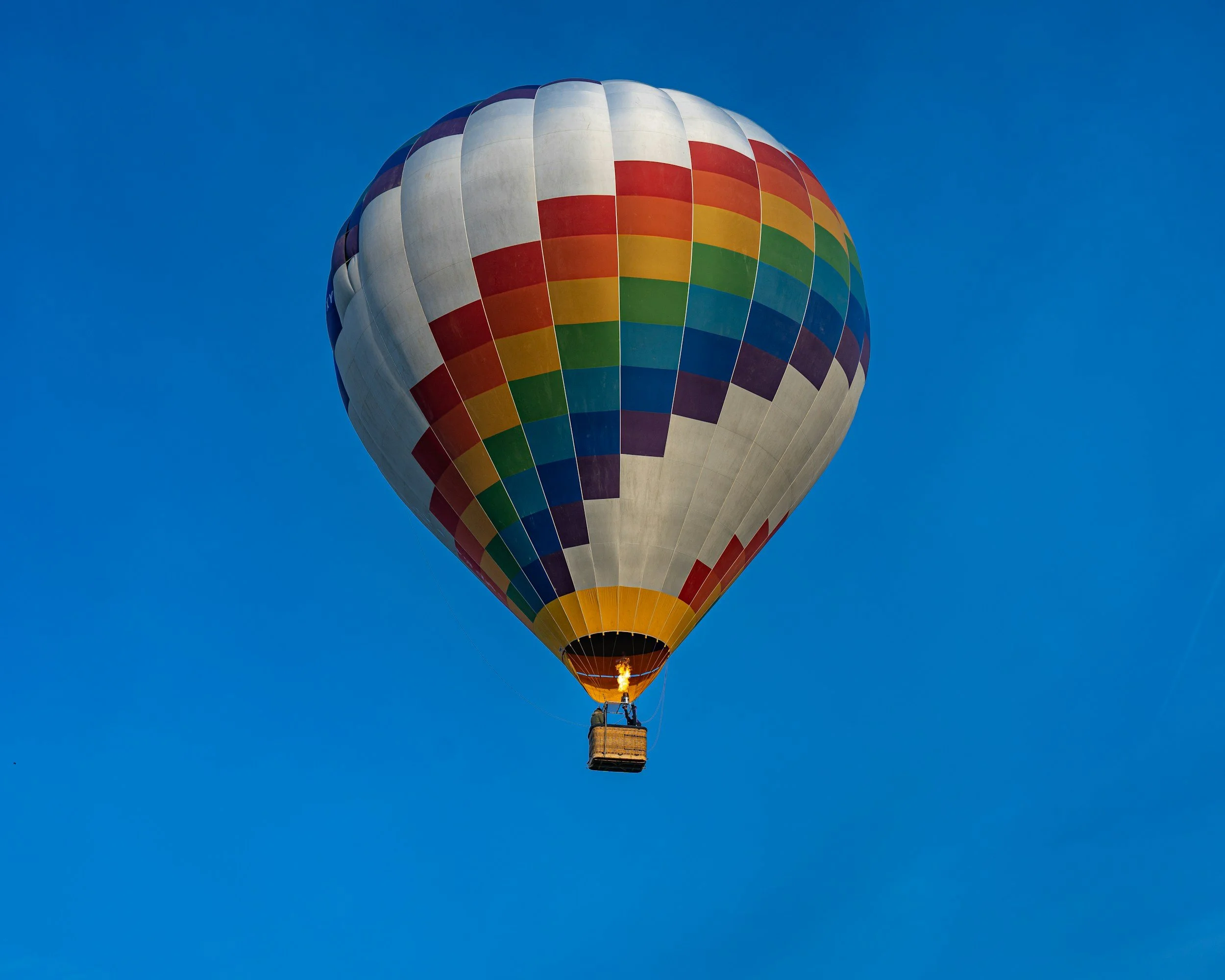Colorful hot air balloon flying in a clear blue sky.