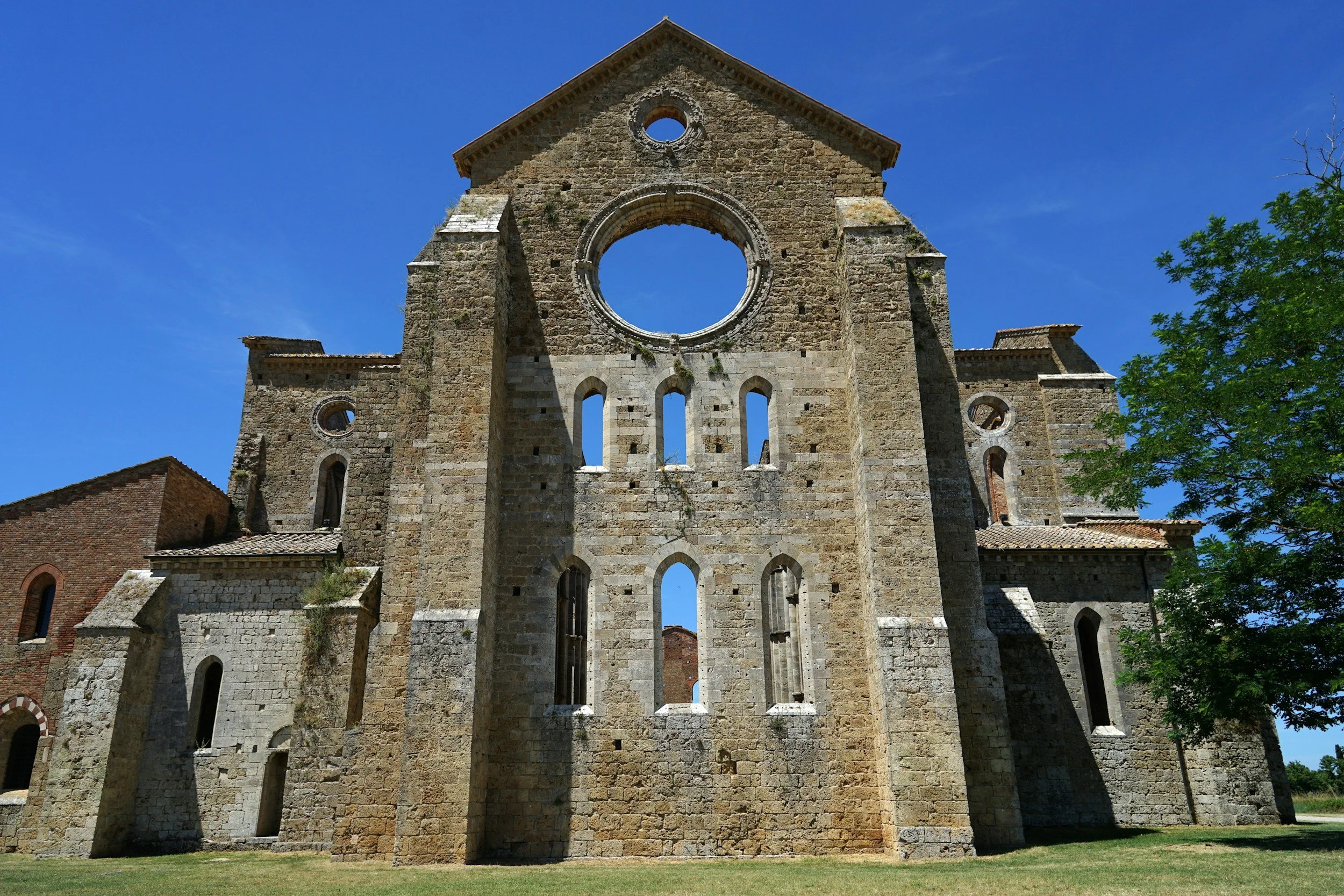 Ancient stone church ruins with large circular window and tall narrow windows, set against a blue sky with green trees nearby.