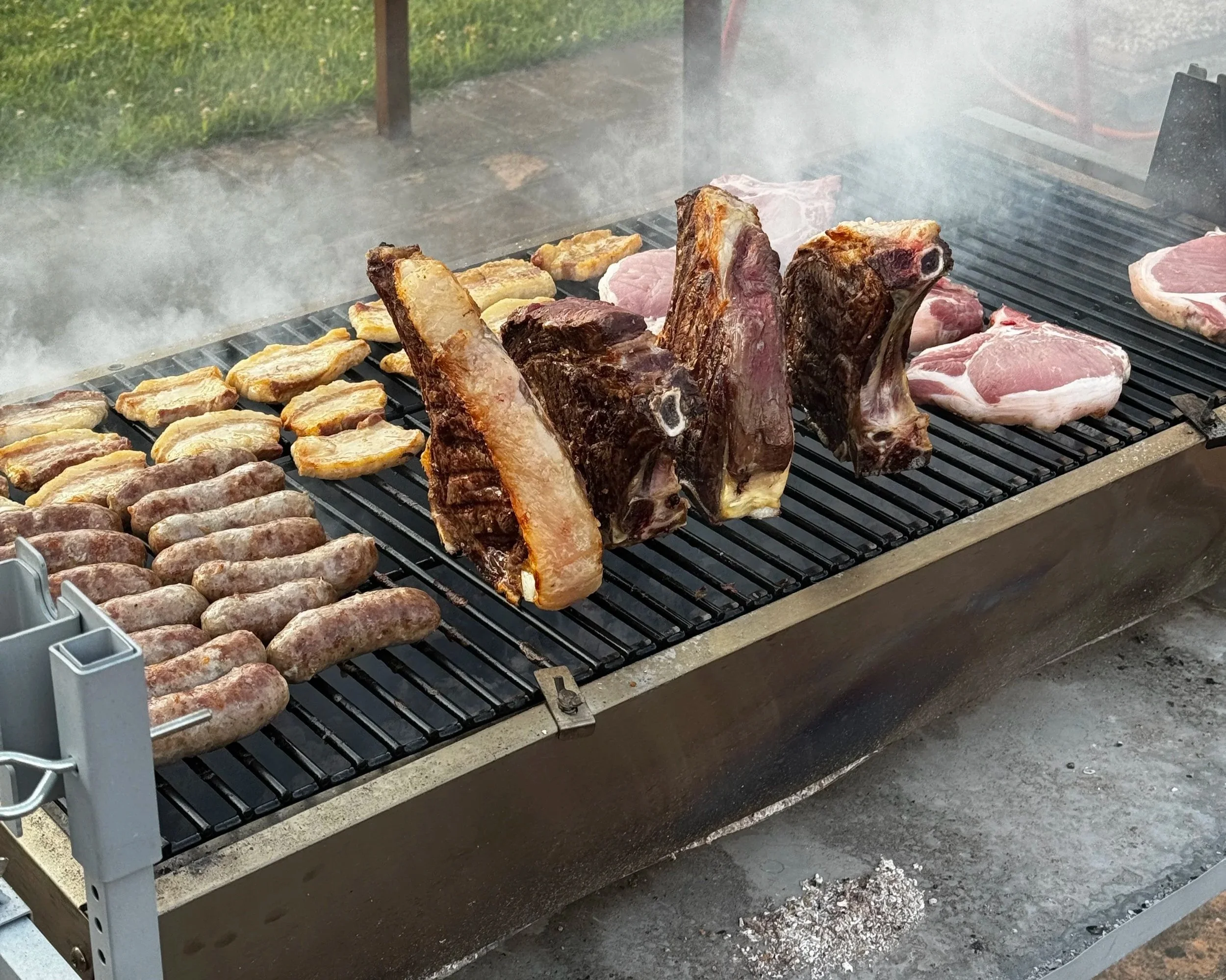 Meat and sausages cooking on a barbecue grill with smoke rising.