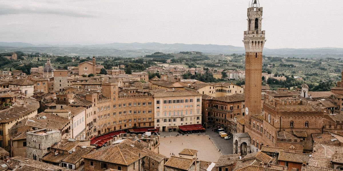 Panoramic view of the historic Piazza della Signoria in Florence, Italy, featuring the Palazzo Vecchio with its tall bell tower, surrounded by medieval buildings with terracotta roofs.