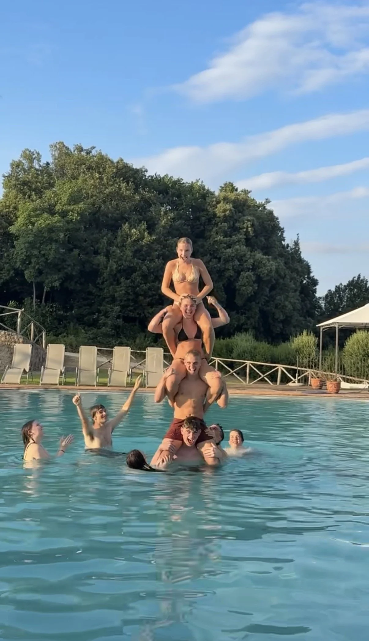 Group of people forming a human tower in a swimming pool outdoors on a sunny day.