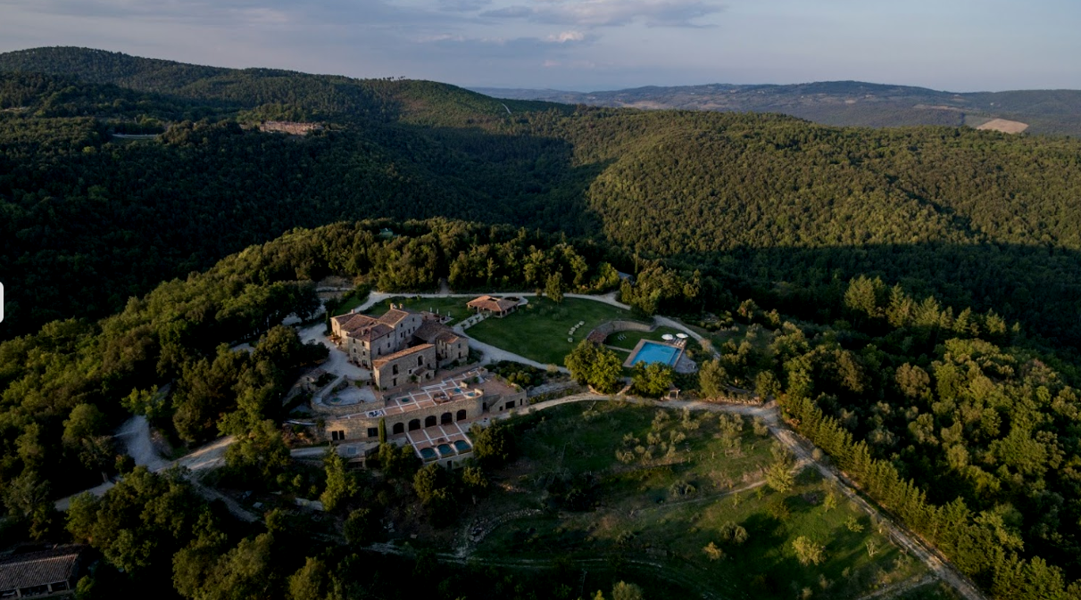 A large estate with a mansion, swimming pool, and surrounding greenery, set in a hilly, forested landscape.