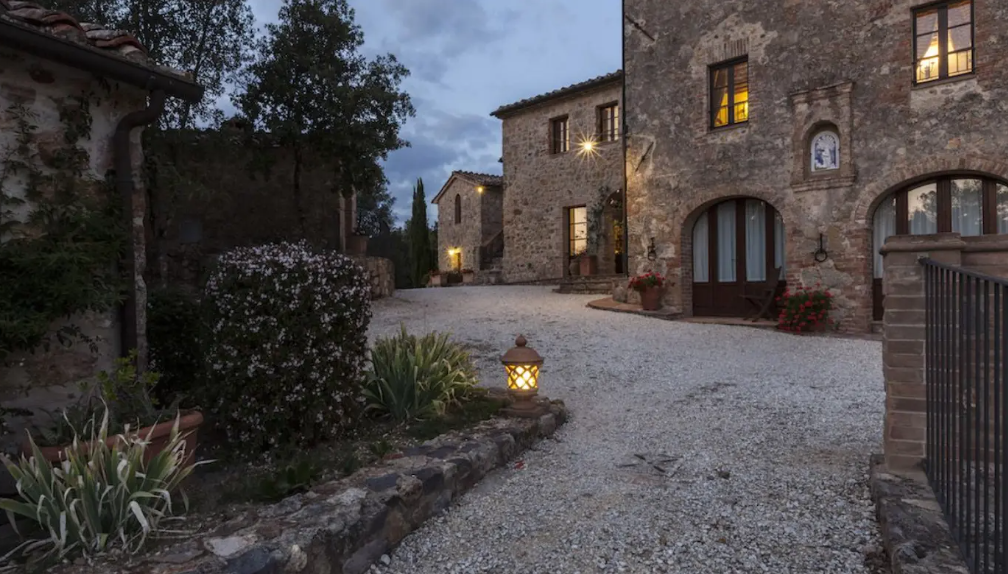A cobblestone driveway leading to stone buildings with illuminated windows during evening time.