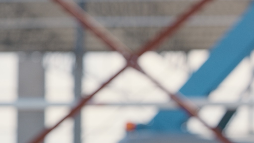 Close-up view of a chain-link fence with blurred construction site and blue sky in the background.