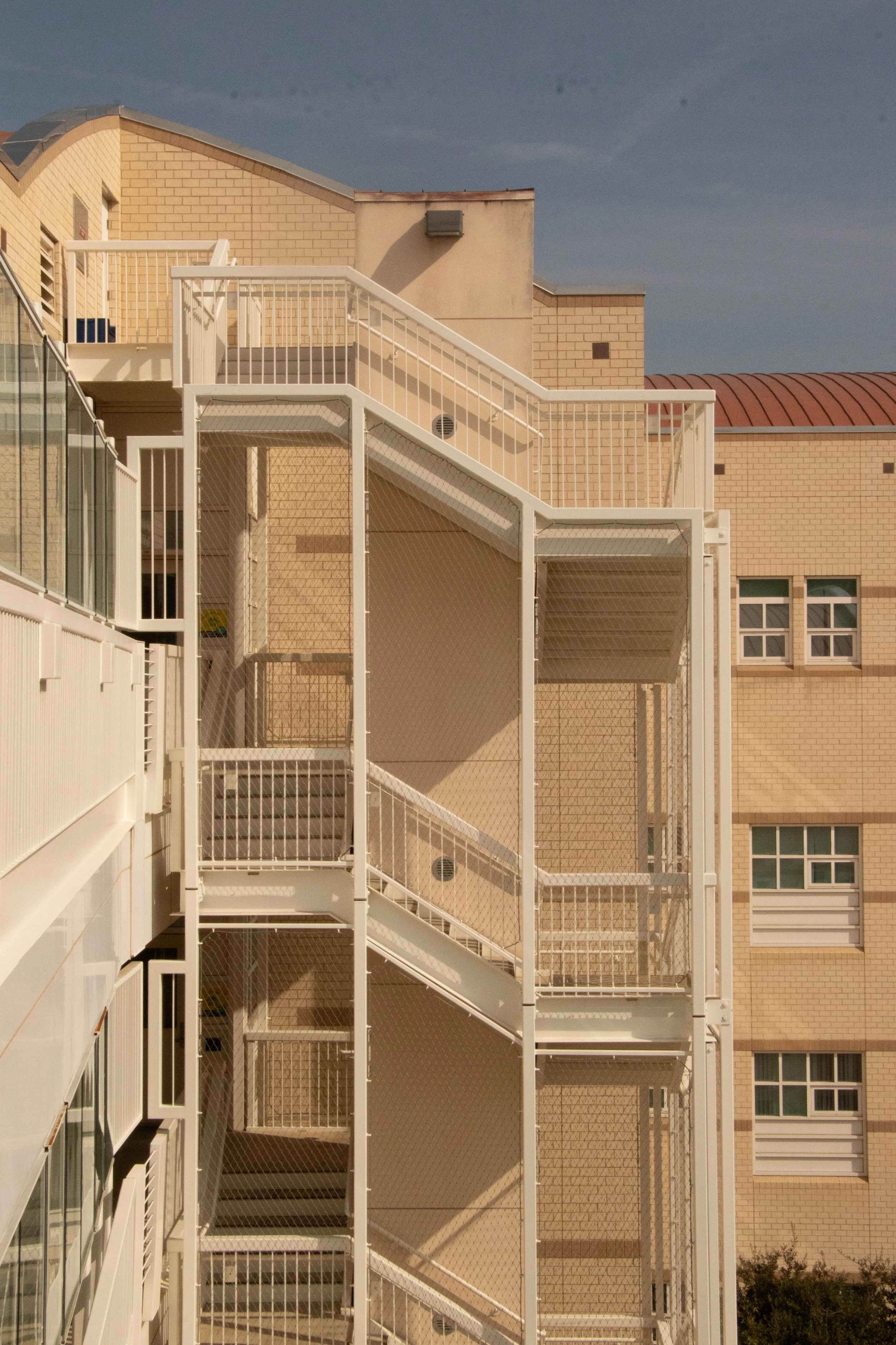 Exterior view of an apartment building with staircases, metal railings, and beige brick walls.