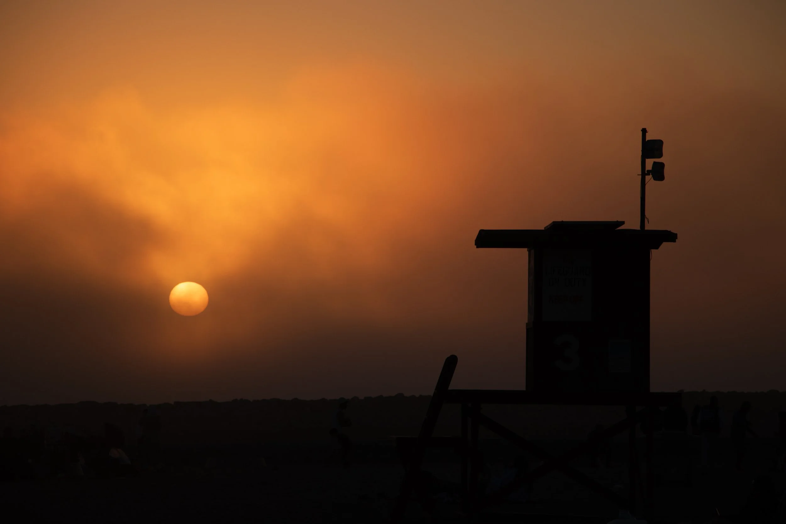 Silhouette of a lifeguard tower on the beach with the sun setting in the background and a sky filled with orange and yellow hues.