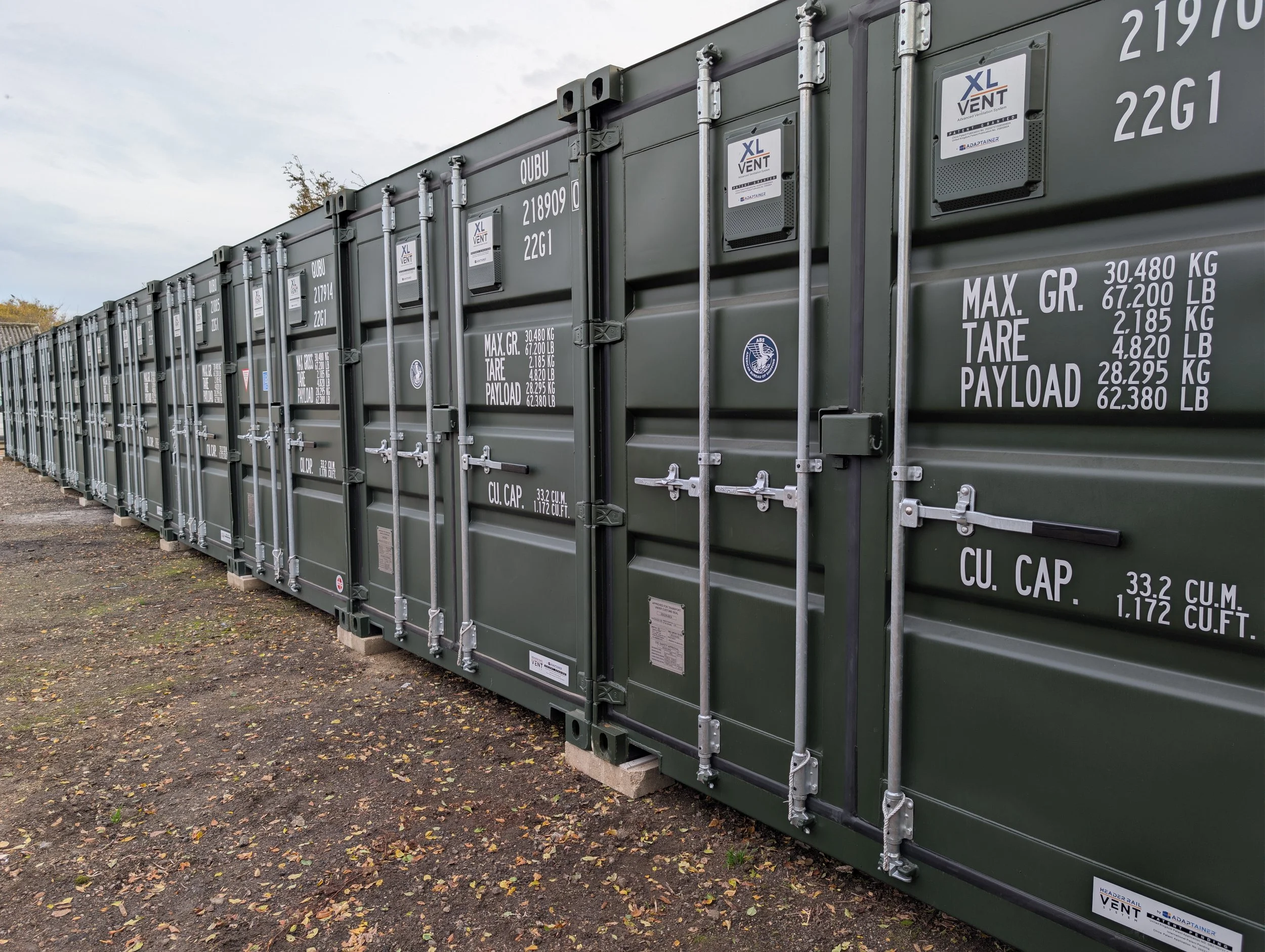 Row of green shipping containers on secure suffolk storage gravel lot.