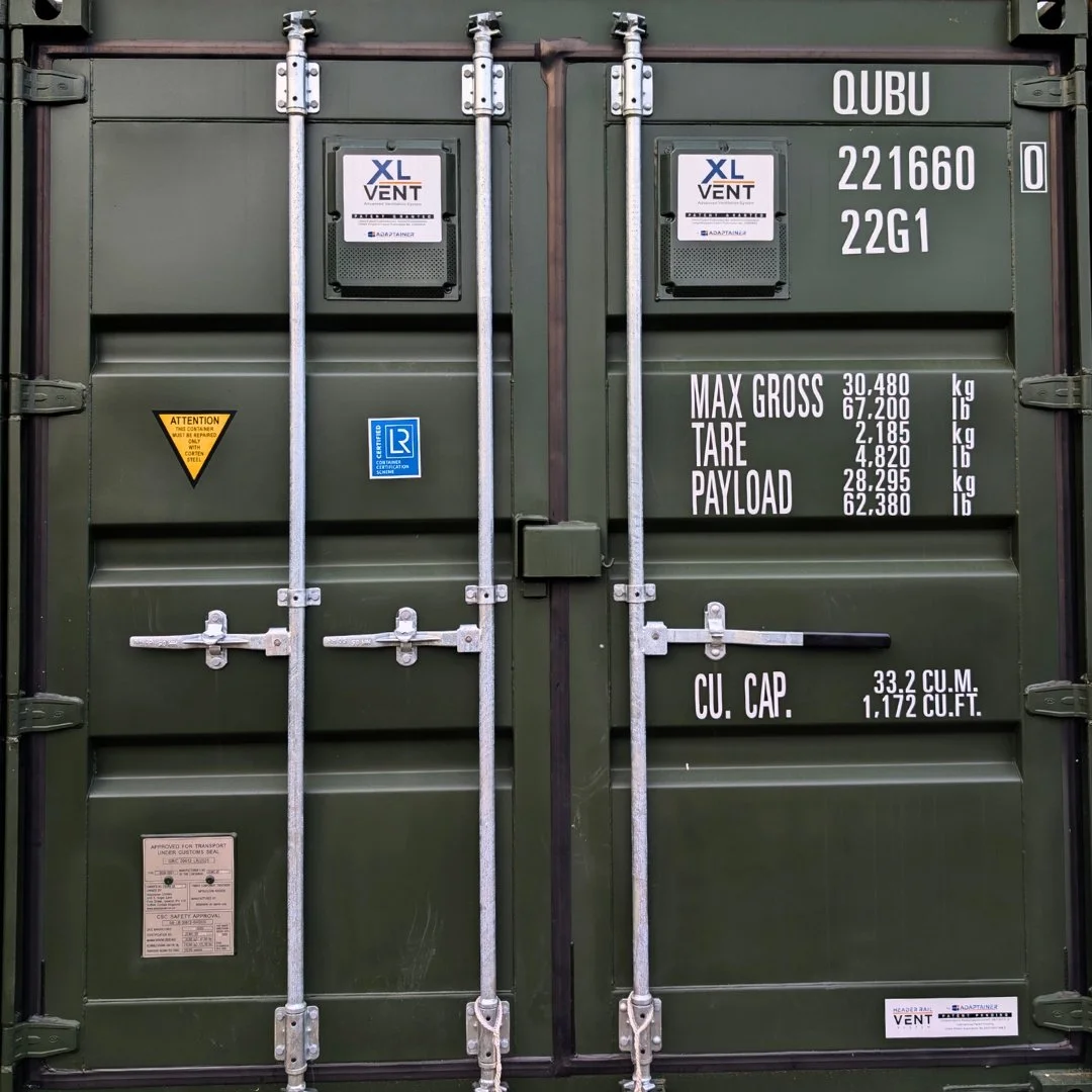 Green secure shipping container with various white and black labels and metal locking mechanisms on the doors.