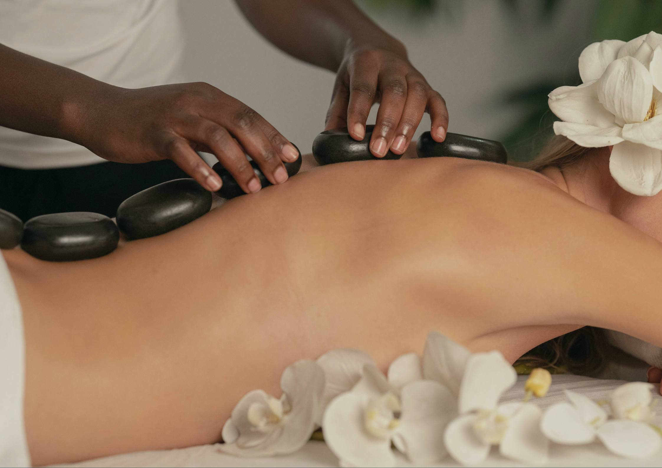 A person receiving a hot stone massage in a spa setting, with a flower decoration nearby.