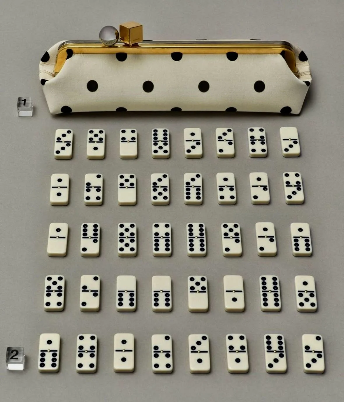 A collection of dominoes arranged in rows, with a polka-dot patterned bag and some decorative items at the top, and two small numbered tags on the left side of the image.