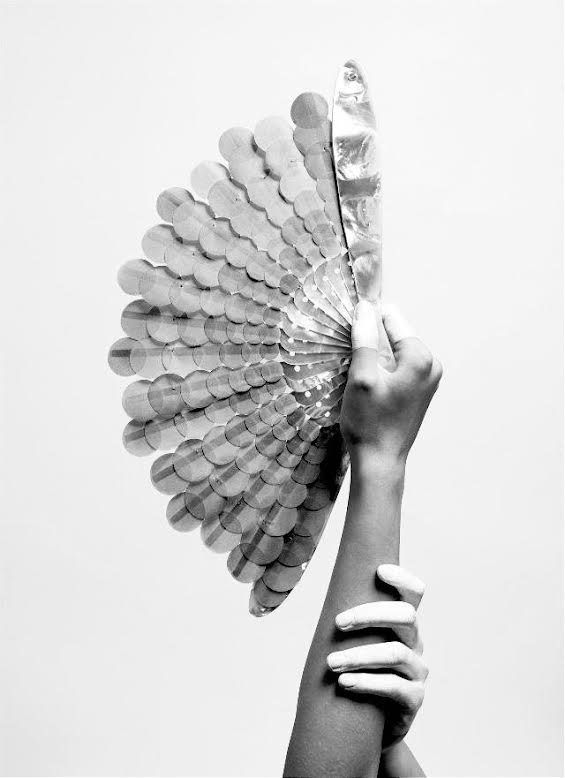 A hand holding a fan made of overlapping paper feathers, creating a wing-like appearance.
