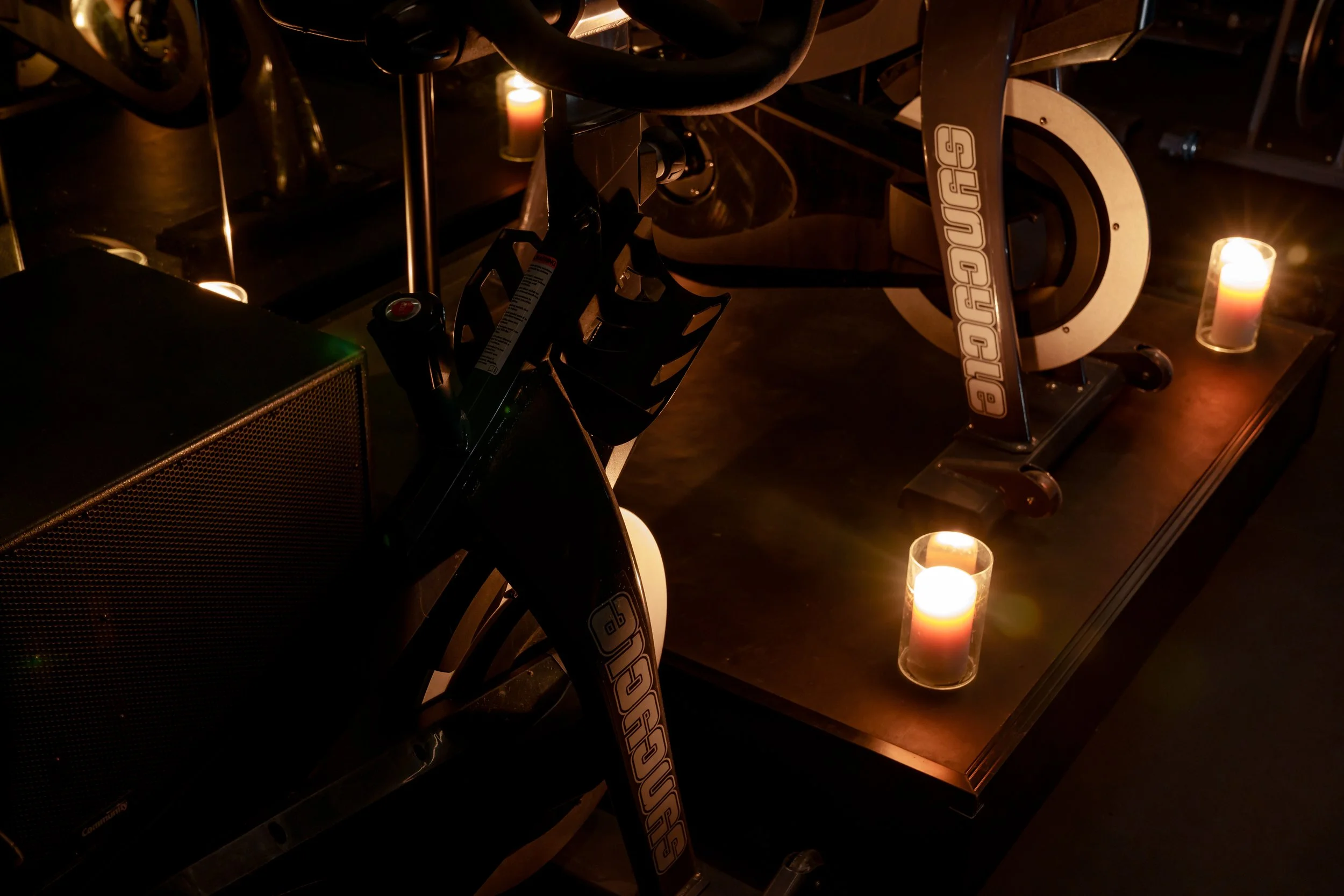 Dimly lit room with a stationary exercise bike labelled Synycle on a platform, surrounded by lit candles in glass holders, creating a cozy ambiance.