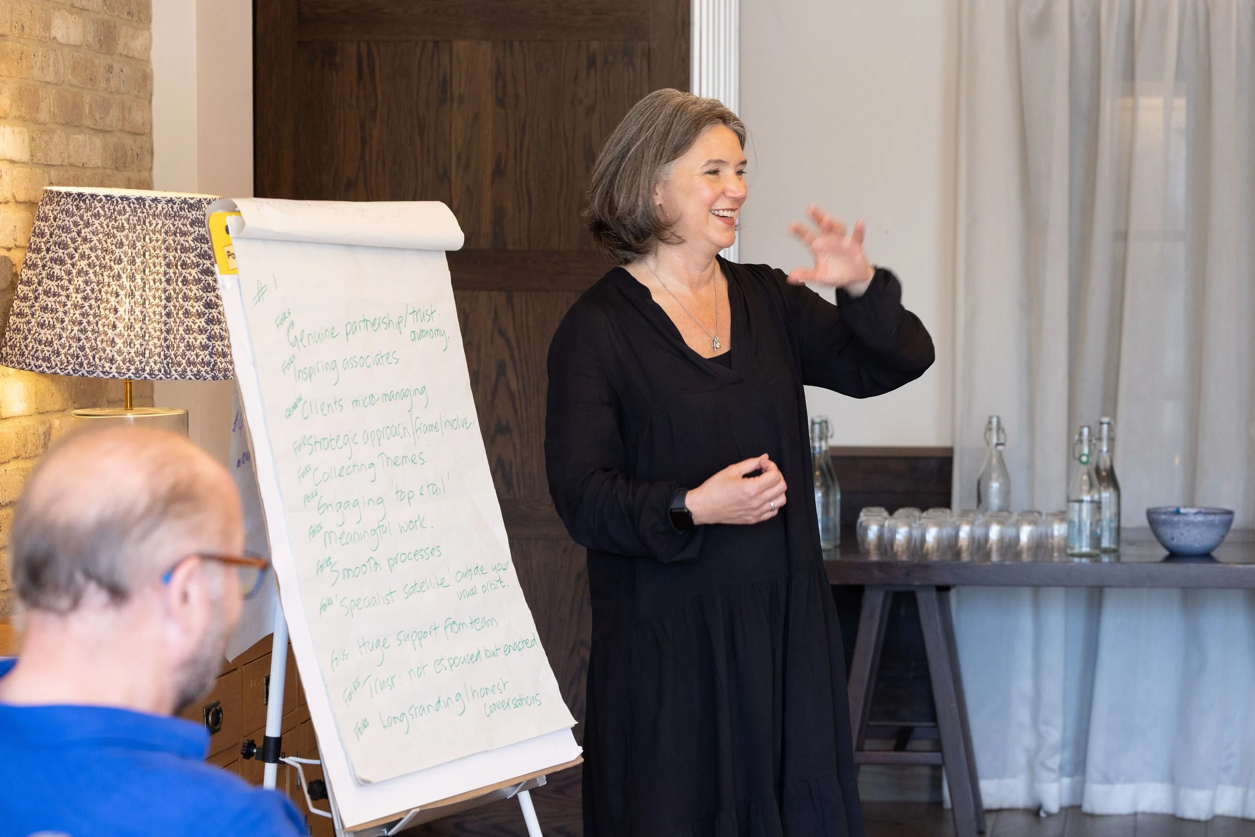 Rebecca Rumsey, executive and leadership coach, standing in front of a flip chart, speaking and gesturing with her hand during a presentation.