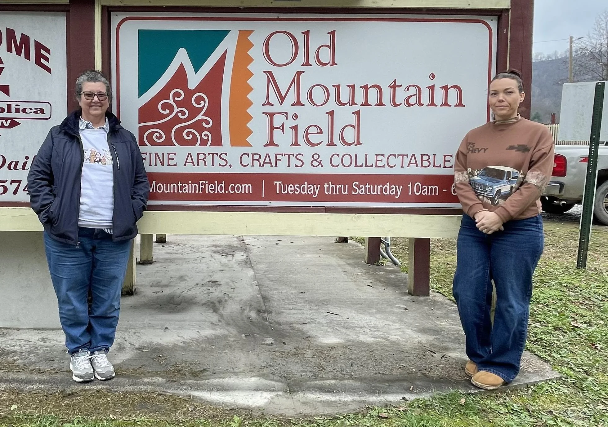 owners of old mountain field fine artrs and craft in matewan, wv standing in front of their sign proudly