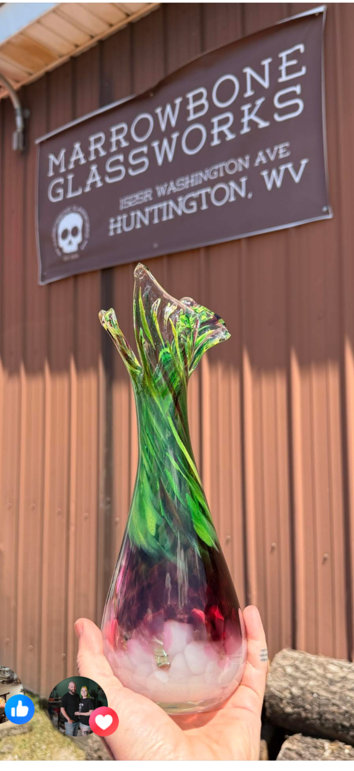a hand holding up the Ramp Vase in front of the modest and sunfaded red metal backdrop of Marrowbone's facade where West Virginia glassblowing heritage is upheld