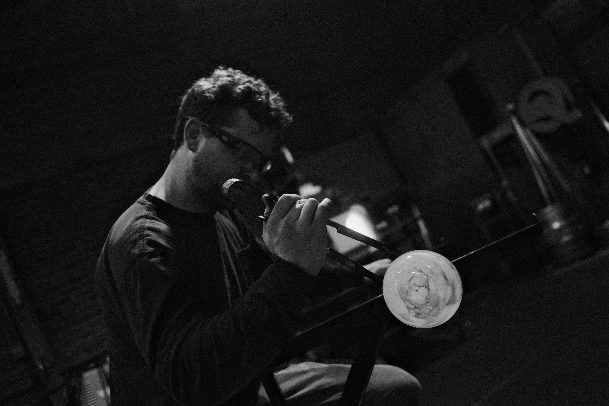 glassblower Jared Neal inflating a hot glass bubble with his breath