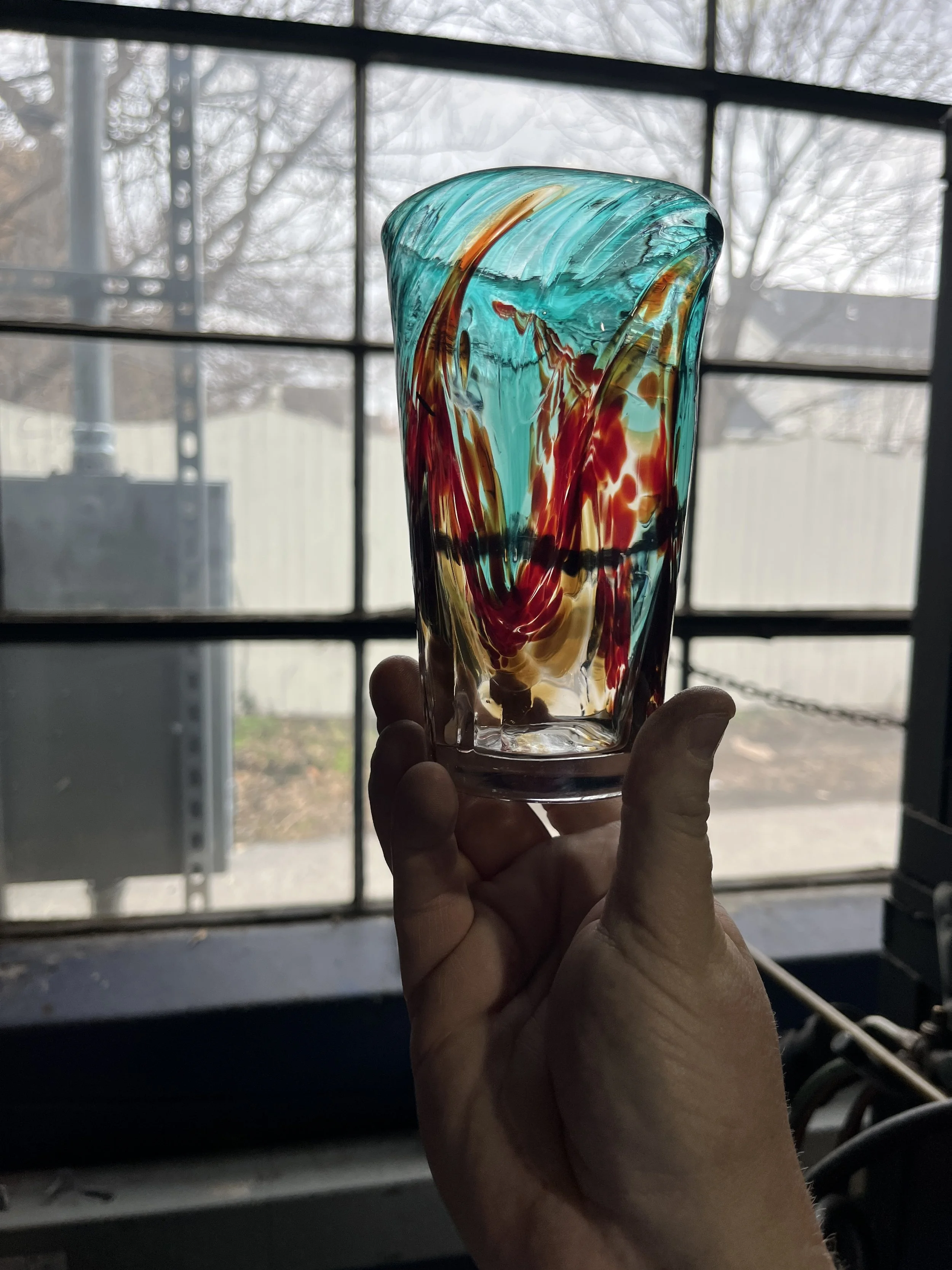 colorful swirl handblown glass pint glass held up to sunlight