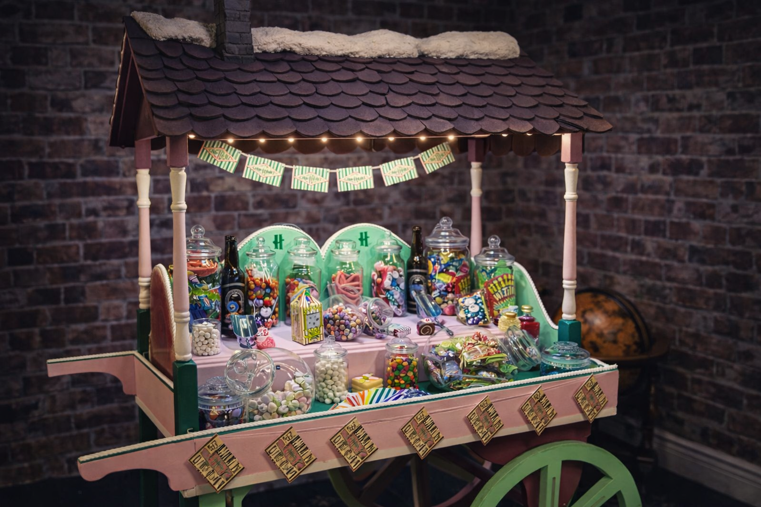 A colourful sweet cart with a pink and green design, filled with jars of assorted candies, themed in the style of Honeydukes sweet shop from Harry Potter.