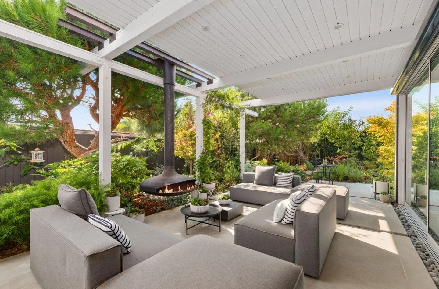 Three wings surround the courtyard, opening to the pool and gardens beyond. A retractable glass wall blurs the line between indoors and out, creating one continuous living space. The covered patio and fireplace extend the experience day and night. Re