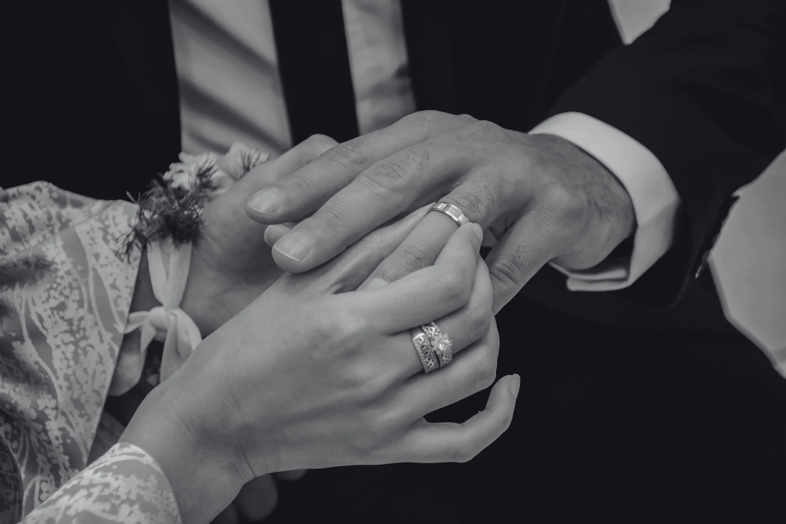 A close-up of a wedding ceremony showing a man and woman holding hands, with their wedding rings prominently displayed, including a wedding band and an engagement ring.