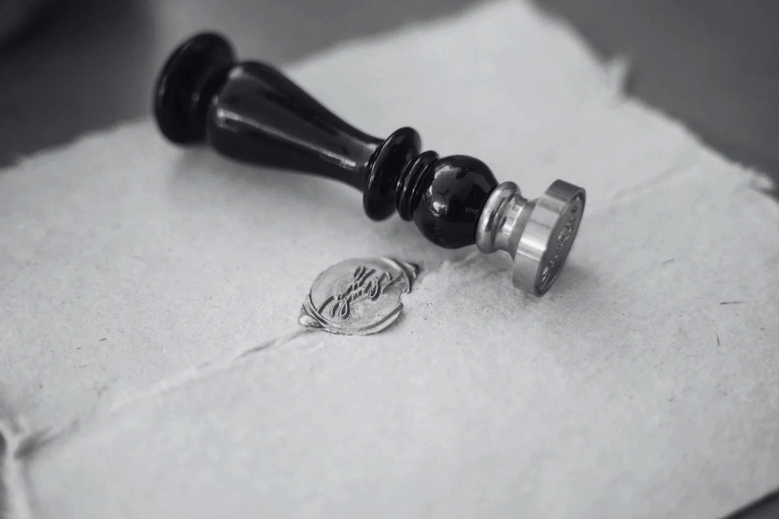 A black and silver vape device lying on a white surface with a small glass vial of liquid and a winding strand of liquid nearby.