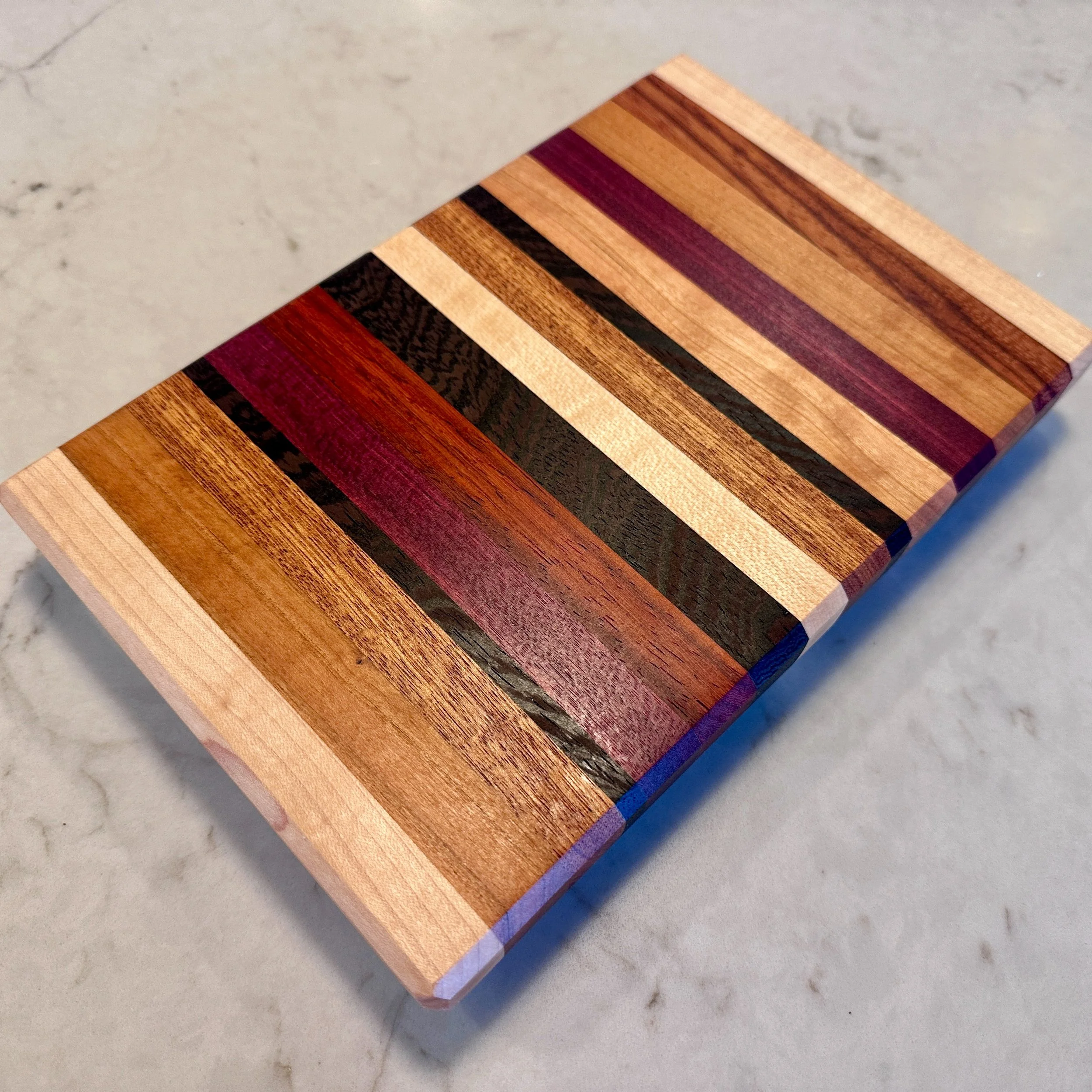 Edge grain cutting board crafted from Maple, Cherry, Walnut, Padauk, Purpleheart, and Ebiara.