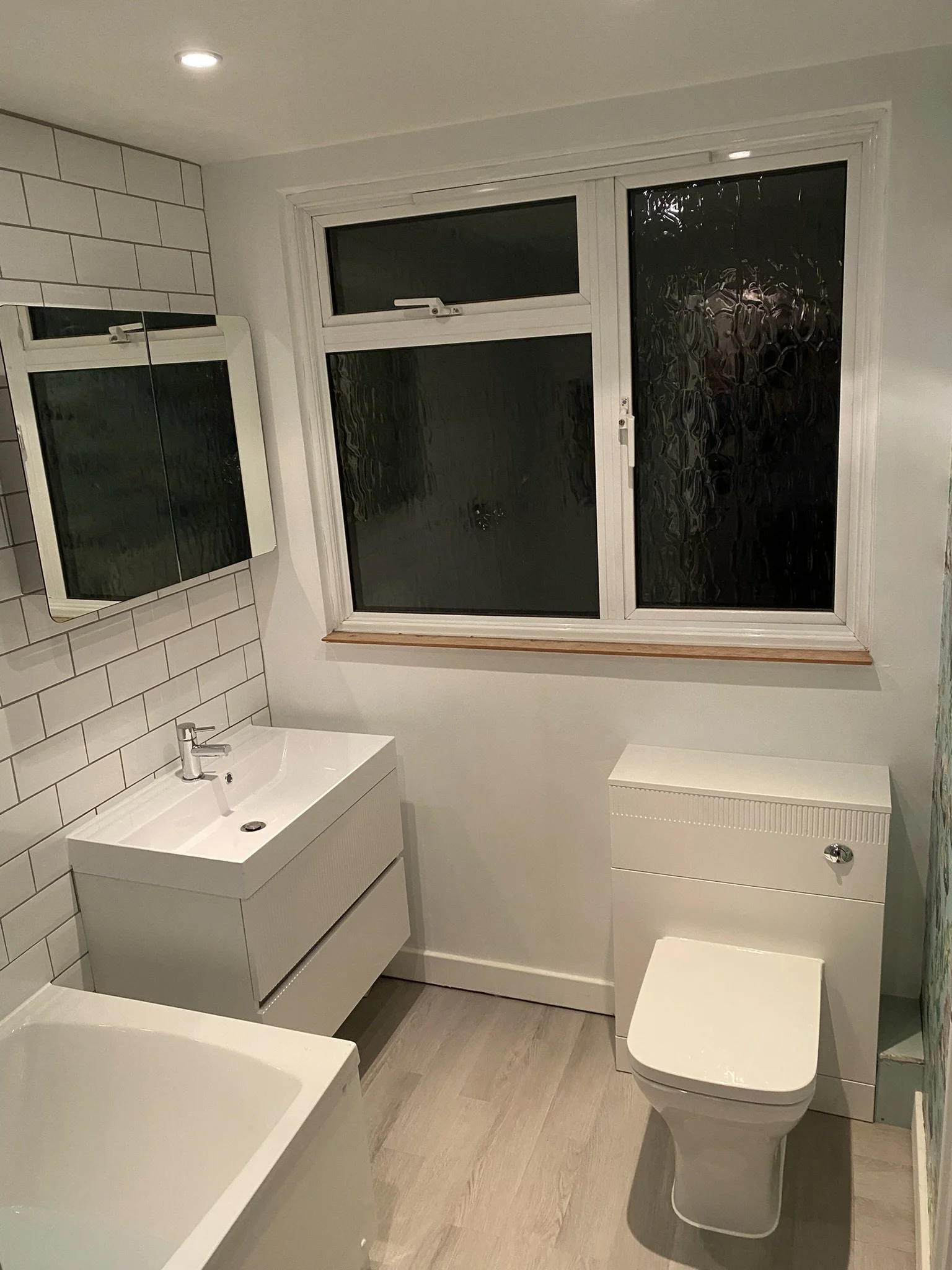 Small bathroom featuring a white vanity with a sink, a mirror cabinet, a toilet, a window with frosted glass, and light-colored flooring.