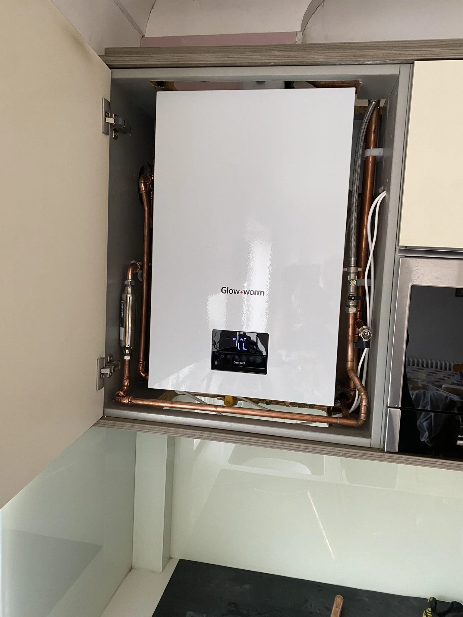 A Glowworm brand boiler installed inside a cabinet with copper pipes and wires visible around it.