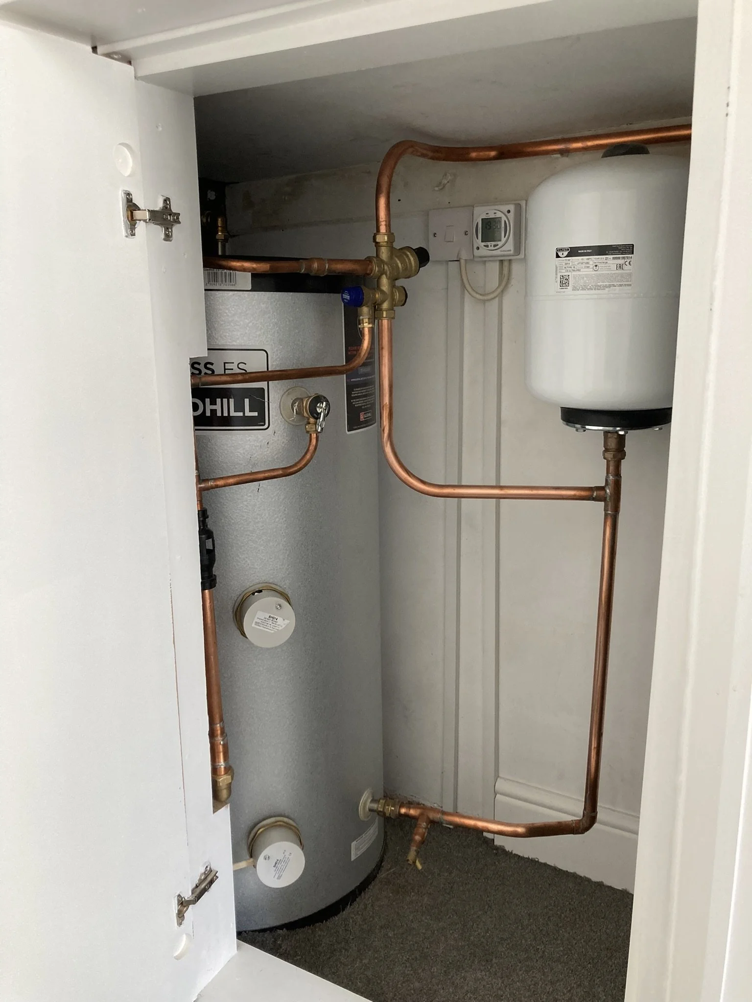 Inside a utility cabinet with a water heater, copper pipes, and a white expansion tank.